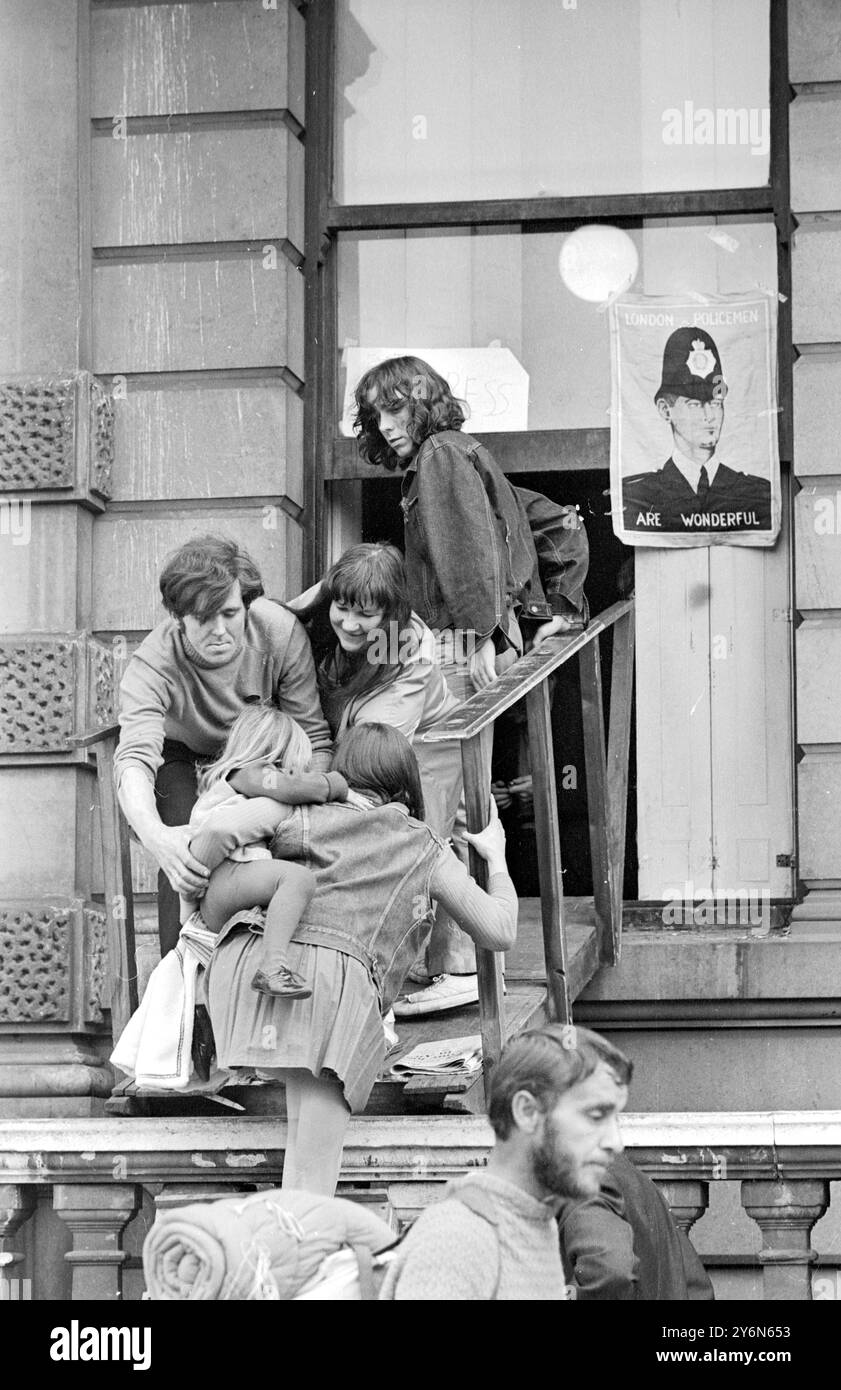 Londres : une femme et un enfant sont assistés par des squatters pour entrer dans le manoir vide de 60 pièces a 144, Piccadilly, Londres, ce matin. Ironiquement, le mur du bâtiment est orné d'une affiche avec le message : «les policiers de Londres sont merveilleux». Les squatters ont repris le bâtiment plus tôt cette semaine, et hier soir, il a été signalé que 350 personnes avaient emménagé dans le bâtiment, qui appartient à Amalgamated West End Developments and Property Trust Ltd Hier, un ultimatum a été donné aux squatters sous la forme d'une ordonnance de la haute cour les obligeant à quitter les lieux avant 1600 heures demain Banque D'Images