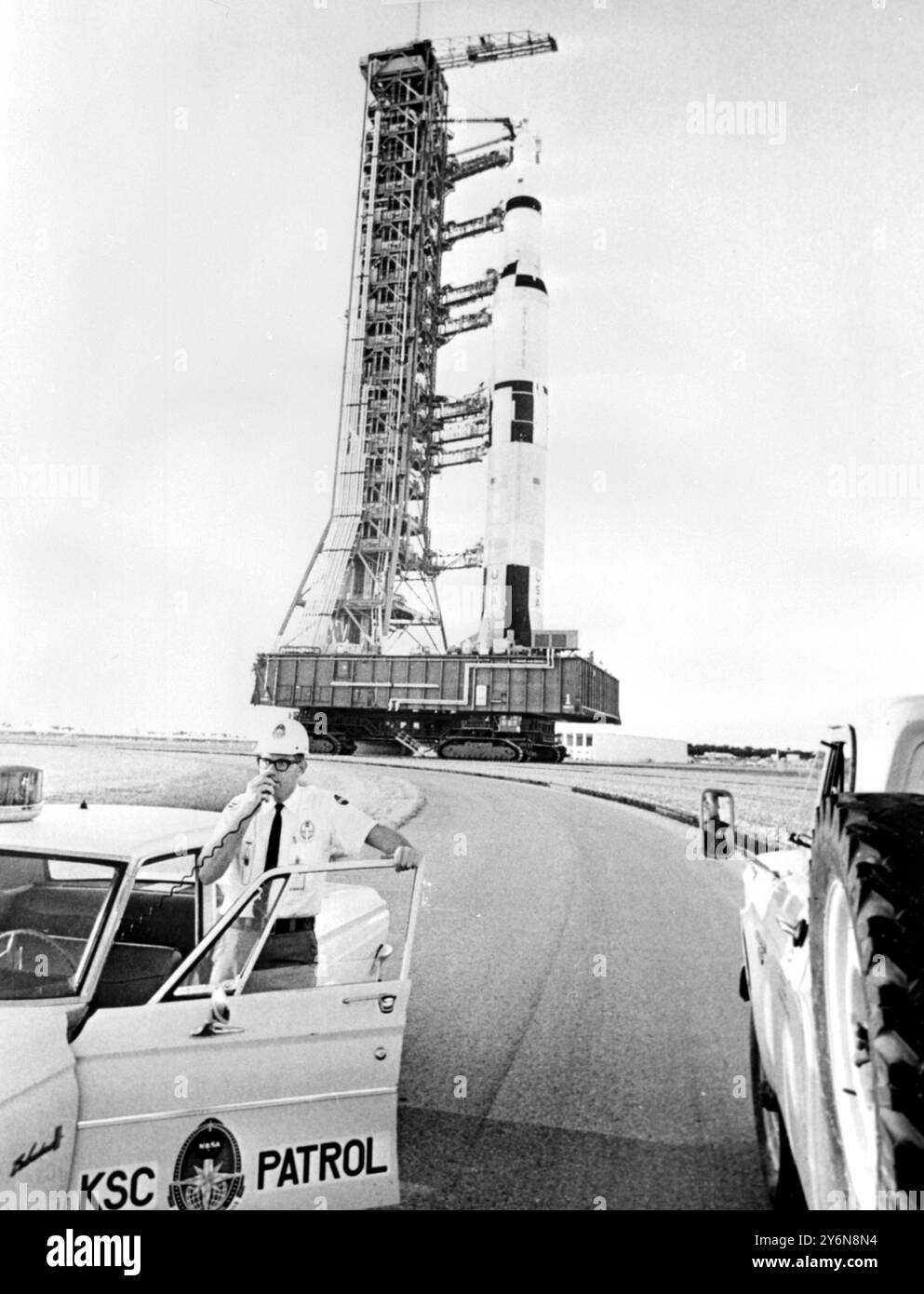 Cape kennedy, Floride : un garde de sécurité dirige les spectateurs et les membres de la presse, alors que derrière lui la première fusée Saturn V américaine sur la lune, le plus puissant du monde monte une énorme tortue comme un tracteur à une allure d'escargots jusqu'à sa rampe de lancement. Alors que la fusée de 364 pieds a été transportée sur les 3 1/2 miles de son bâtiment d'assemblage à son site de tir côté océan, le directeur du programme Apollo, le major-général Samuel C. Phillips, a déclaré que le calendrier de lancement avait été révisé et a noté qu'un navire lunaire en surpoids était un « problème gênant » restant. Le premier essai de tir de la Saturn V est prévu pour SOM Banque D'Images