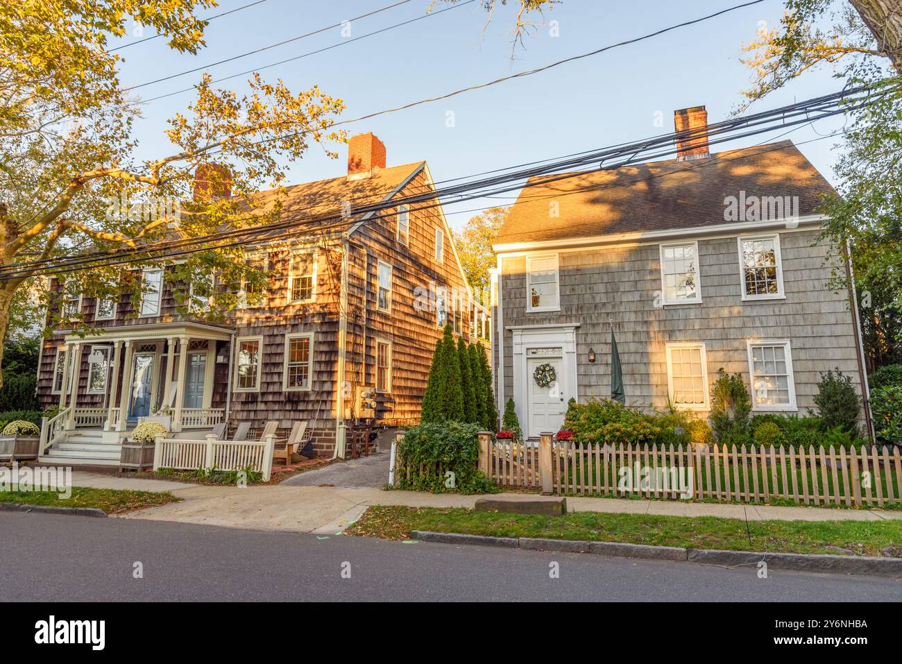 Maisons boisées historiques avec gradens avant clôturés le long d'une rue sous ciel clair au coucher du soleil Banque D'Images