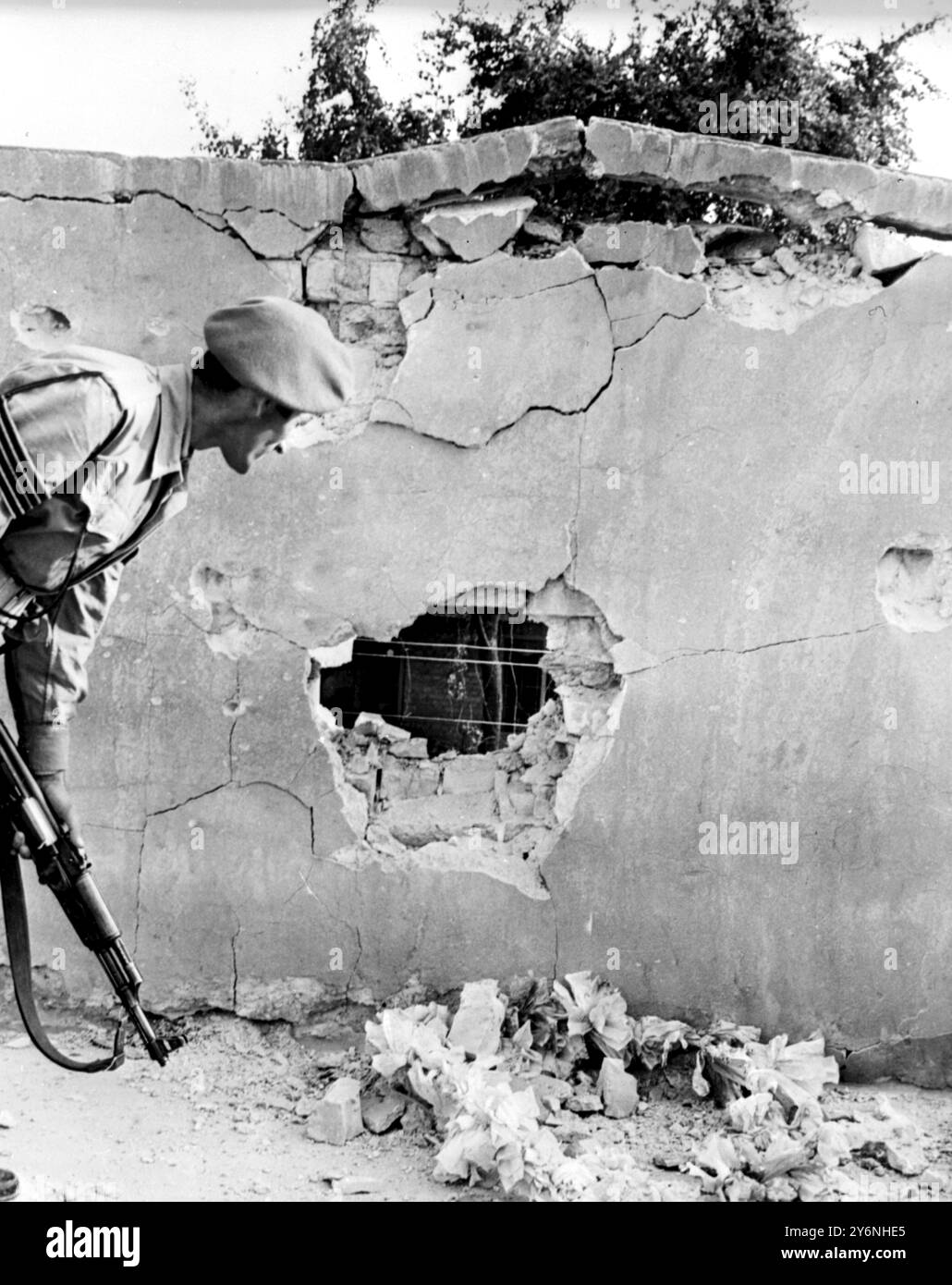 Bagdad, Irak : un soldat du gouvernement inspecte ce trou qui a soufflé dans le mur entourant le quartier général de la Garde nationale baathiste lors des combats entre les troupes gouvernementales et les gardes nationaux pendant le coup d'État du 18 novembre ici, lorsque le parti baathiste au pouvoir a été chassé du pouvoir. Le quartier général était l'un des principaux points à Bahdad sur lesquels les troupes gouvernementales se sont concentrées pendant les combats de rue qui ont suivi l'annonce de la prise de contrôle de l'armée. 27 novembre 1963 Banque D'Images Bagdad, Irak : un soldat du gouvernement inspecte ce trou qui a soufflé dans le mur entourant le quartier général de la Garde nationale baathiste lors des combats entre les troupes gouvernementales et les gardes nationaux pendant le coup d'État du 18 novembre ici, lorsque le parti baathiste au pouvoir a été chassé du pouvoir. Le quartier général était l'un des principaux points à Bahdad sur lesquels les troupes gouvernementales se sont concentrées pendant les combats de rue qui ont suivi l'annonce de la prise de contrôle de l'armée. 27 novembre 1963 Banque D'Images