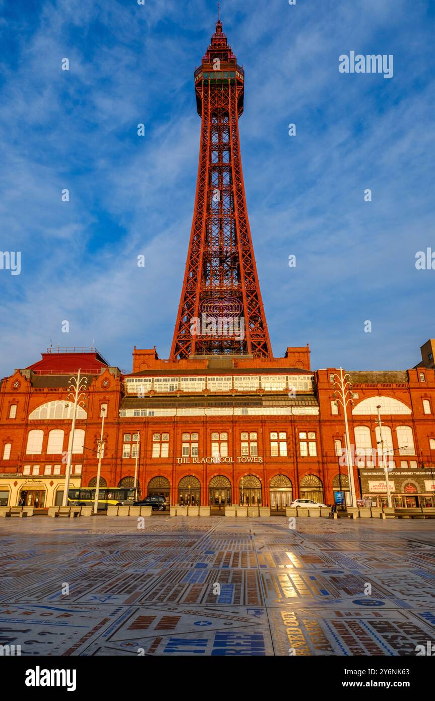 La tour emblématique de Blackpool baignée par la lumière du coucher du soleil, avec la façade du bâtiment historique et la promenade à motifs. Banque D'Images