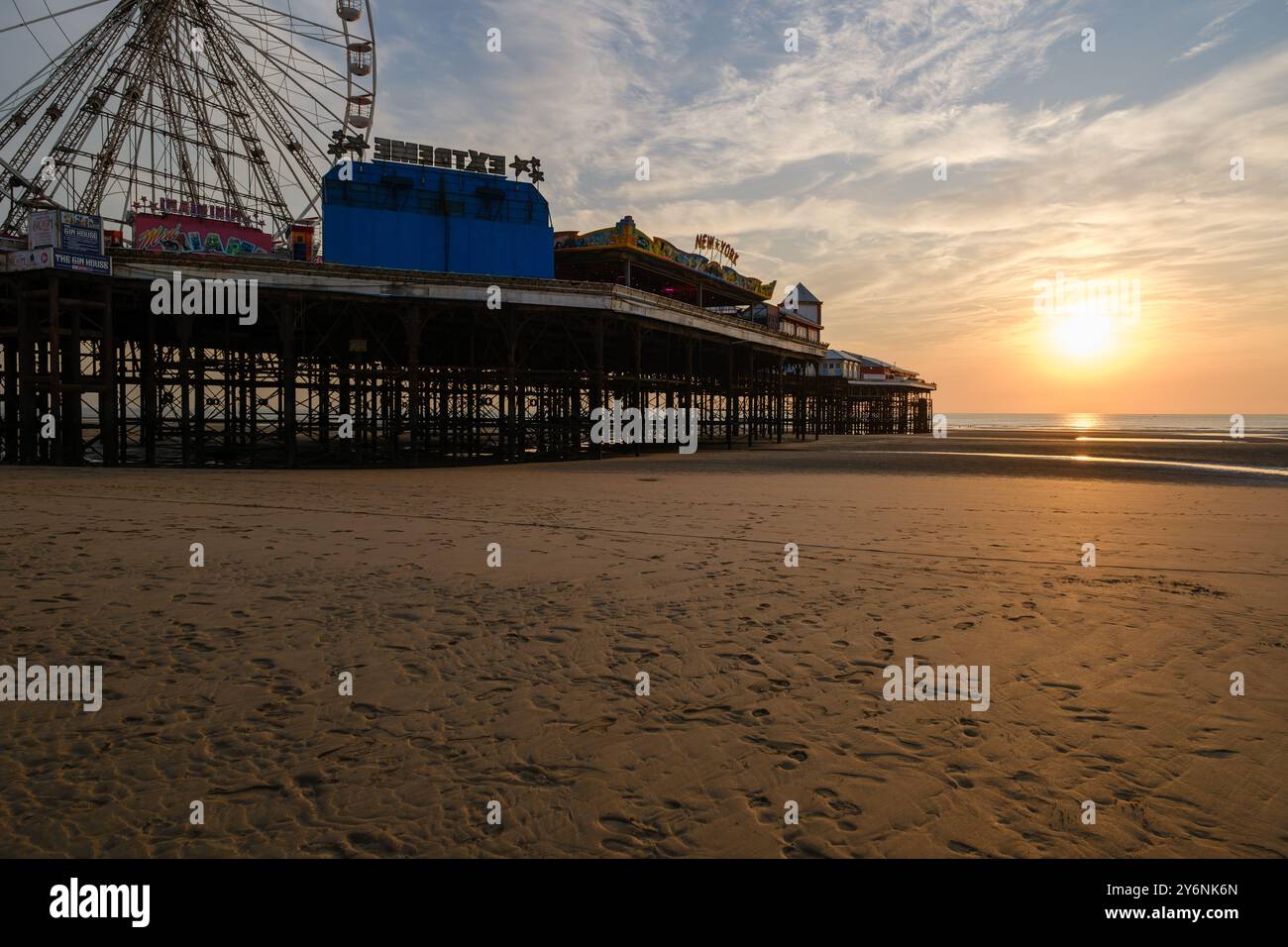 Vue sereine sur le coucher du soleil avec une grande roue et un parc d'attractions sur une jetée, projetant de longues ombres sur la plage. Banque D'Images