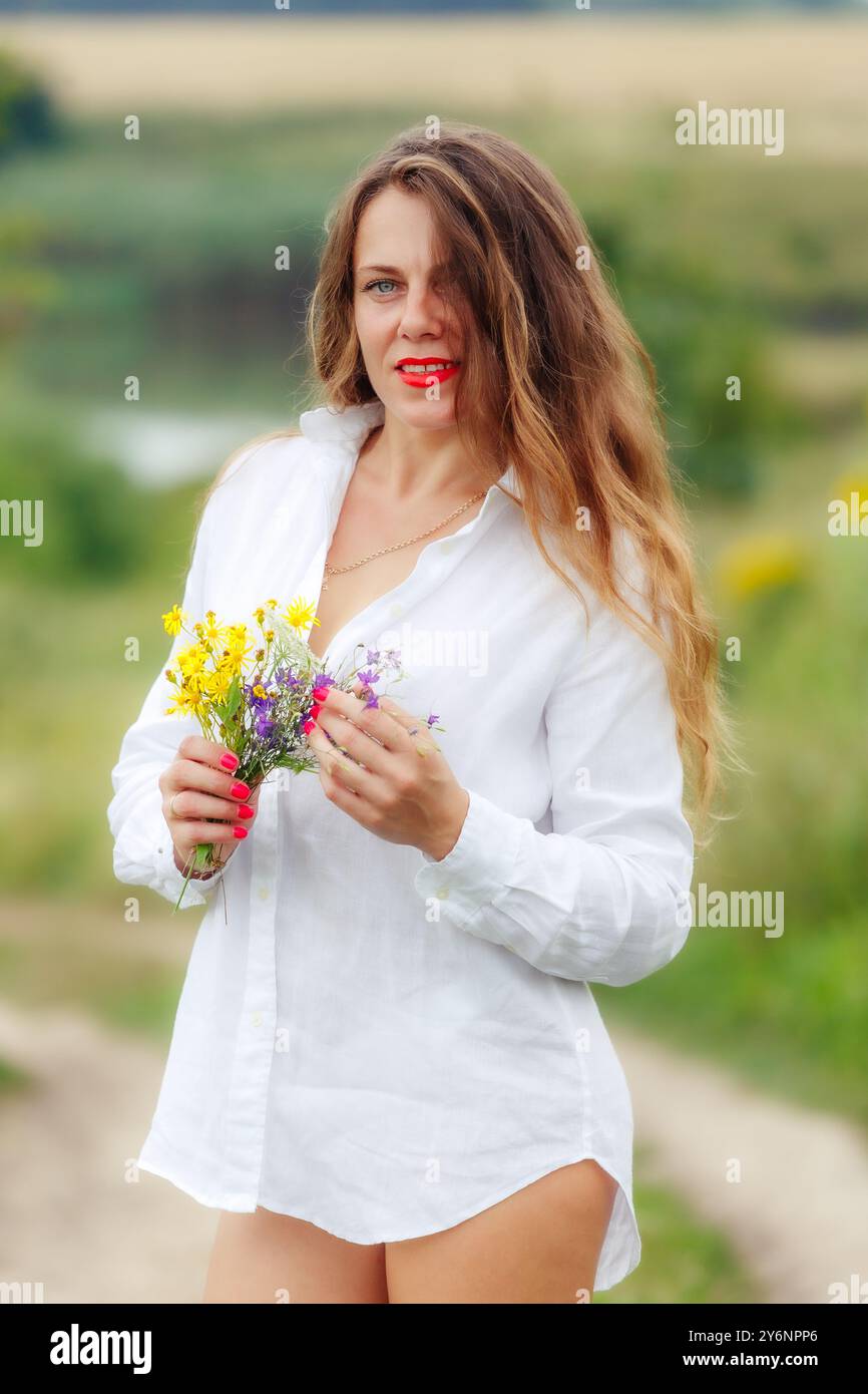 Douce belle jeune femme profitant du soleil, tenant un bouquet de fleurs sauvages. Une charmante fille avec un bouquet de fleurs sauvages. Photo de l'offre estivale. Banque D'Images