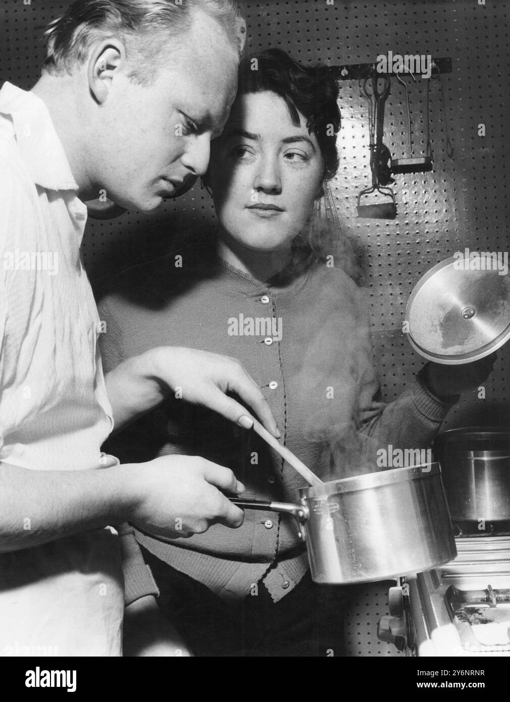 L'homme cuisine tandis que sa femme regarde 1959 Banque D'Images