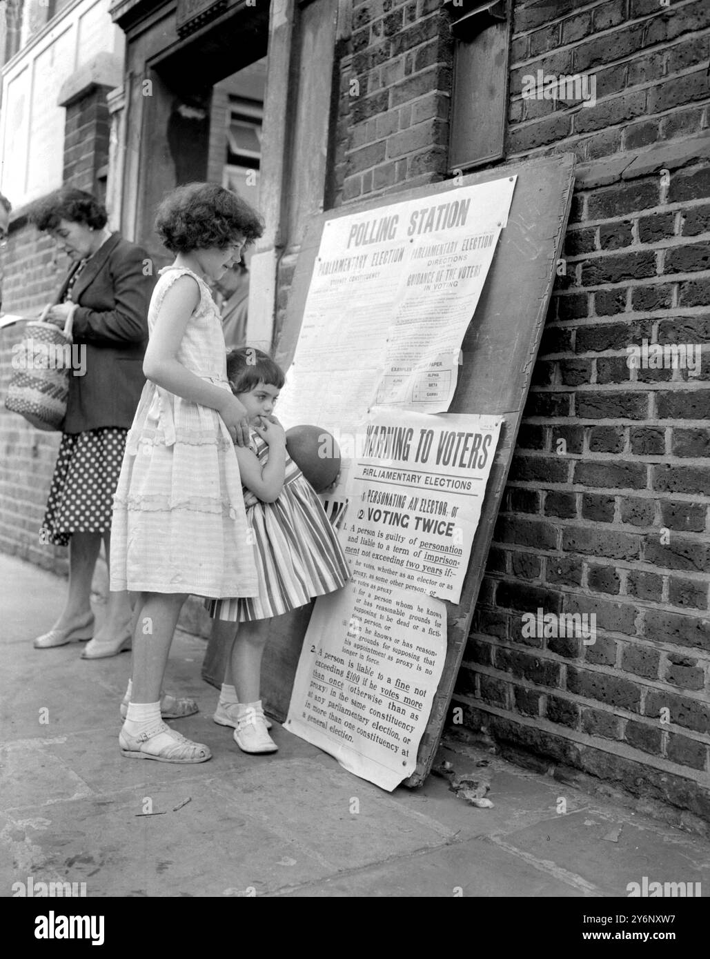Londres : les sœurs Connie, 12 ans et Joany Spiteri, 4 ans, se tiennent devant leur école à Ashfield Street, Stepney, essayant de travailler sur Election Business. Pas d'école aujourd'hui car elle a été reprise pour Polling Station. 8 octobre 1959 Banque D'Images