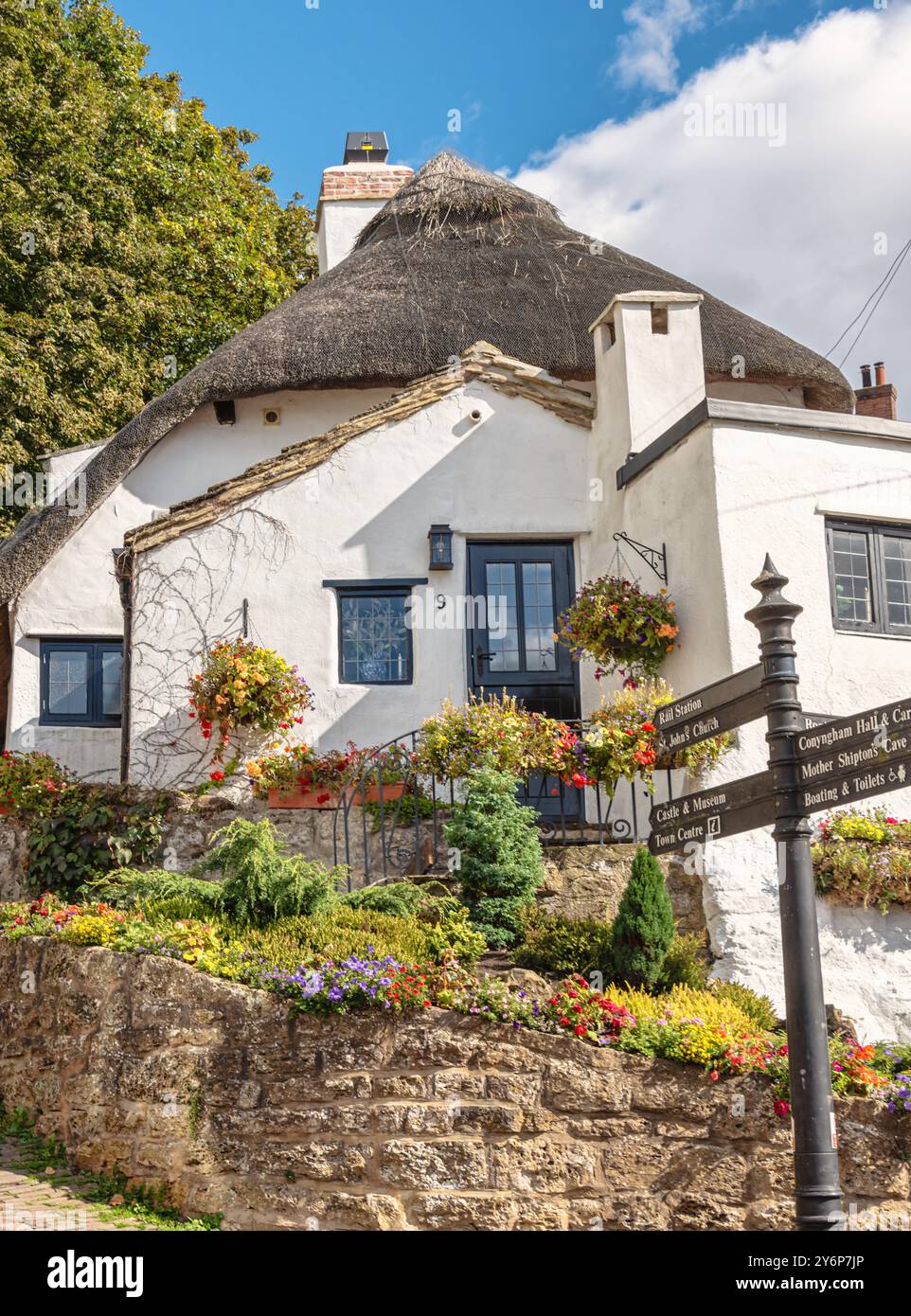 Une maison avec un toit de chaume se dresse sur un terrain d'angle avec une rocaille pleine de fleurs colorées. Un panneau est au premier plan et un ciel avec nuage i Banque D'Images