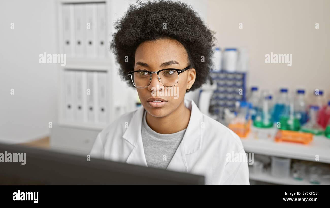 Scientifique afro-américaine focalisée travaillant dans un laboratoire, entourée d'équipement. Banque D'Images