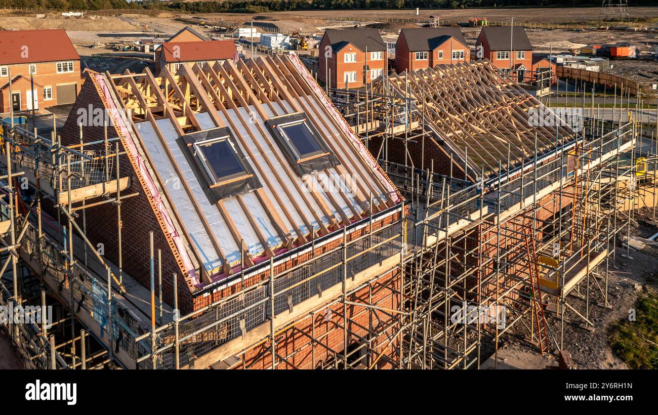 Vue aérienne d'un toit en construction avec poutres et apex supportant des fenêtres de puits de lumière extérieures sur une maison neuve entourée d'échafaudages sur un Banque D'Images Vue aérienne d'un toit en construction avec poutres et apex supportant des fenêtres de puits de lumière extérieures sur une maison neuve entourée d'échafaudages sur un Banque D'Images