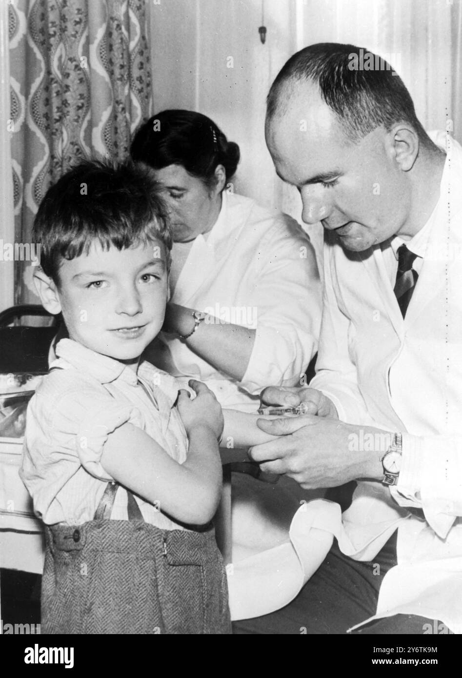 HULL, Yorkshire : Nicholas Pearcy, neuf ans, tient la manche tandis que le Dr Garey se prépare à lui faire une injection anti-polio à la clinique Collman Street à Hull hier. Il y a eu une augmentation alarmante du nombre de victimes de poliomyélite dans la ville au cours des dernières semaines, 15 nouveaux cas depuis la fin septembre. Mercredi prochain, pour la première fois en Grande-Bretagne, une vaccination orale de masse sera administrée. Le nouveau vaccin recevra deux gouttes à la fois sur des morceaux de sucre et il est revendiqué pour donner une protection immédiate. 14 OCTOBRE 1961 Banque D'Images