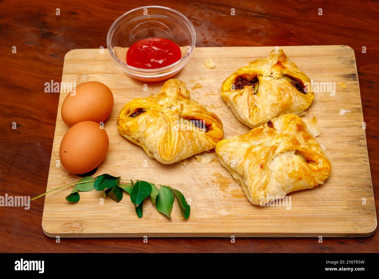 Gros plan sur une planche à découper en feuilletés aux œufs savoureux de style Kerala avec sauce tomate, feuilles de curry et oeuf. Fond en bois Banque D'Images