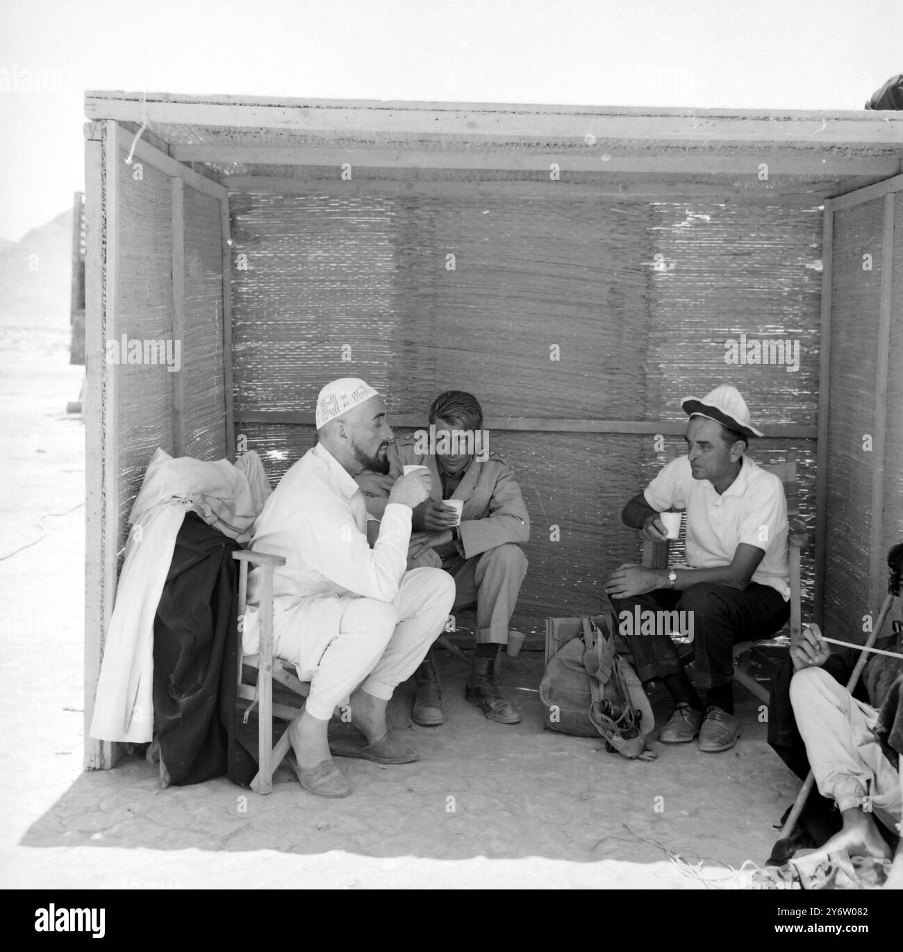 L'HOMME DANS LE CRÂNE Cap Jordan : Une figurine blanche dans un crâne dégustez un verre rafraîchissant avec l'acteur Peter O'Toole, au centre, et le réalisateur David Lean, à droite, dans une cabane installée au cœur du désert jordanien, où se déroule actuellement le tournage de Lawrence d'Arabie. L'homme dans la casquette du crâne ? Sir Alec Guinness, qui joue le prince Feisal dans le film. Peter O'Toole sera vu dans le rôle de Lawrence et le film est produit par Sam Spiegel qui, avec Sir Alec et Mr Lean a réalisé le pont sur la rivière Kwai. 9 AOÛT 1961 Banque D'Images