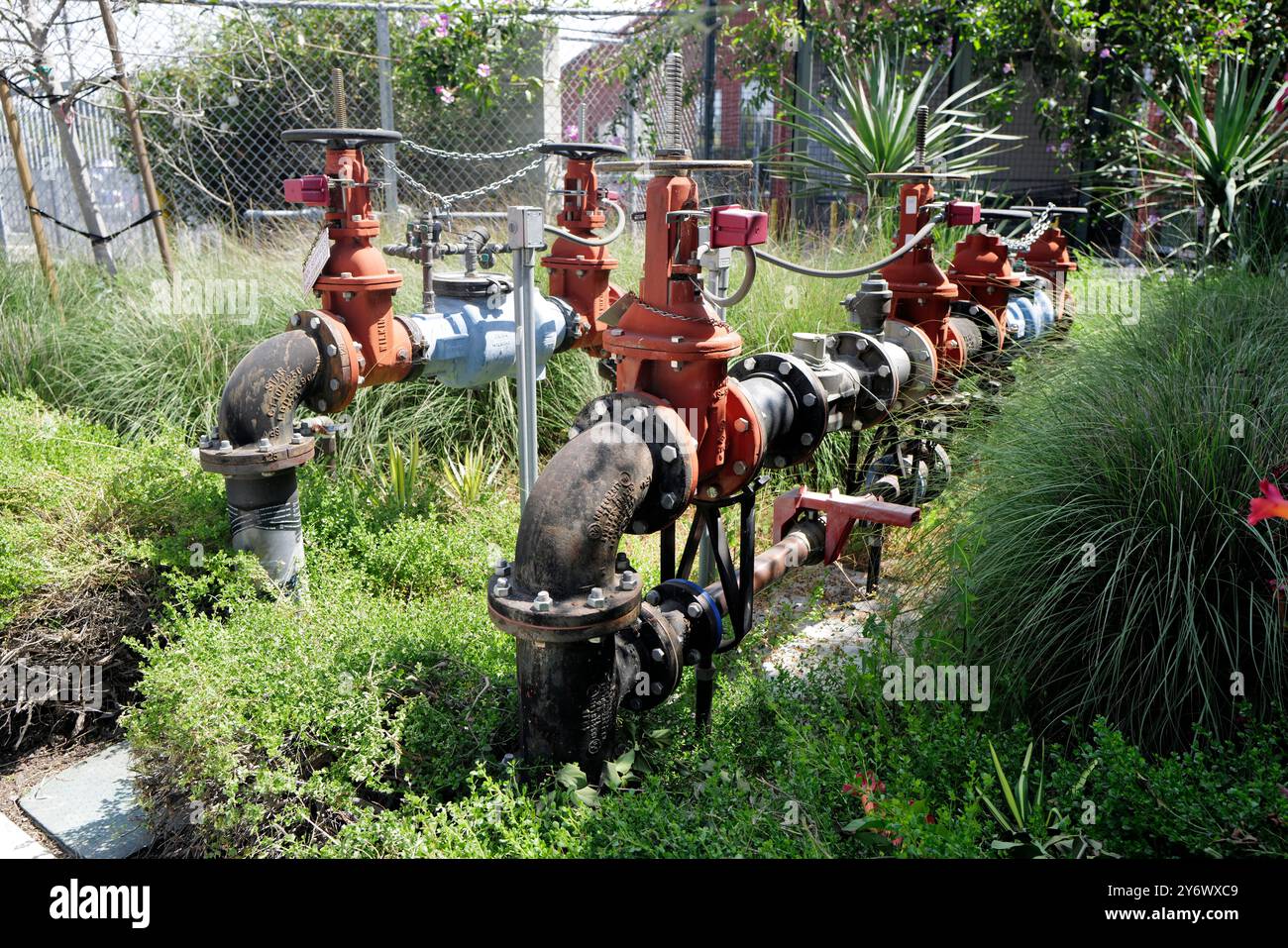 Installation extérieure de vannes d'eau industrielles et de tuyauterie dans une zone paysagée avec de l'herbe et des arbustes, sécurisée par une clôture à maillons de chaîne en arrière-plan Banque D'Images
