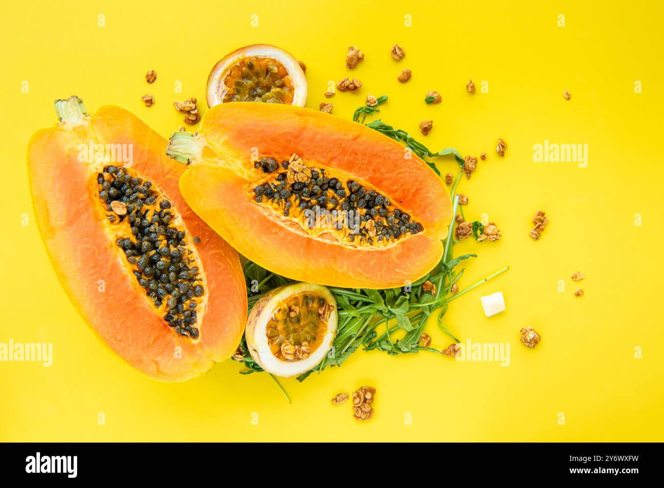 Papaye, fruit de la passion, rucola et granola sur fond jaune. Tranches de papaye sucrée, fruit de la passion, rucola entouré de flocons de granola sur jaune Banque D'Images