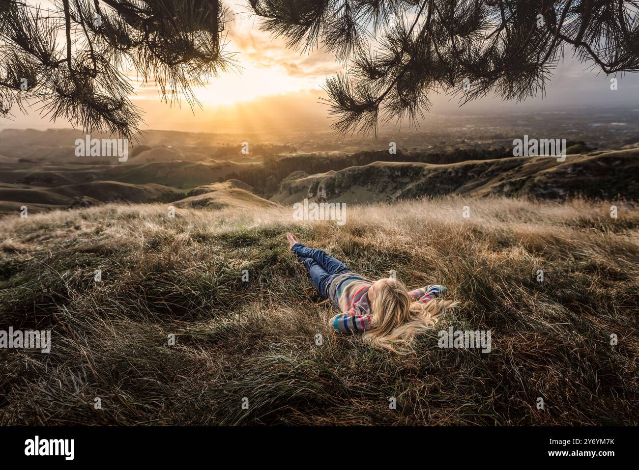 Adolescent allongé dans l'herbe sur le sommet d'une colline dans la lumière dorée Banque D'Images
