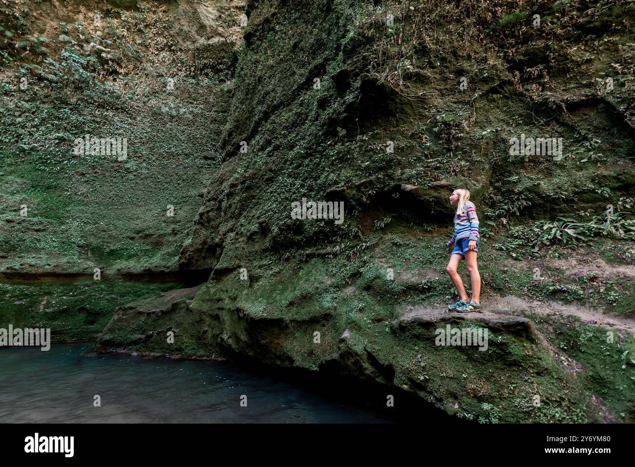 Fille grimpant sur le côté d'une falaise verte au-dessus de l'eau Banque D'Images