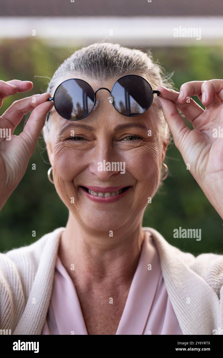 Ajustement des lunettes de soleil, femme souriante profitant d'une journée ensoleillée à l'extérieur, à la maison Banque D'Images