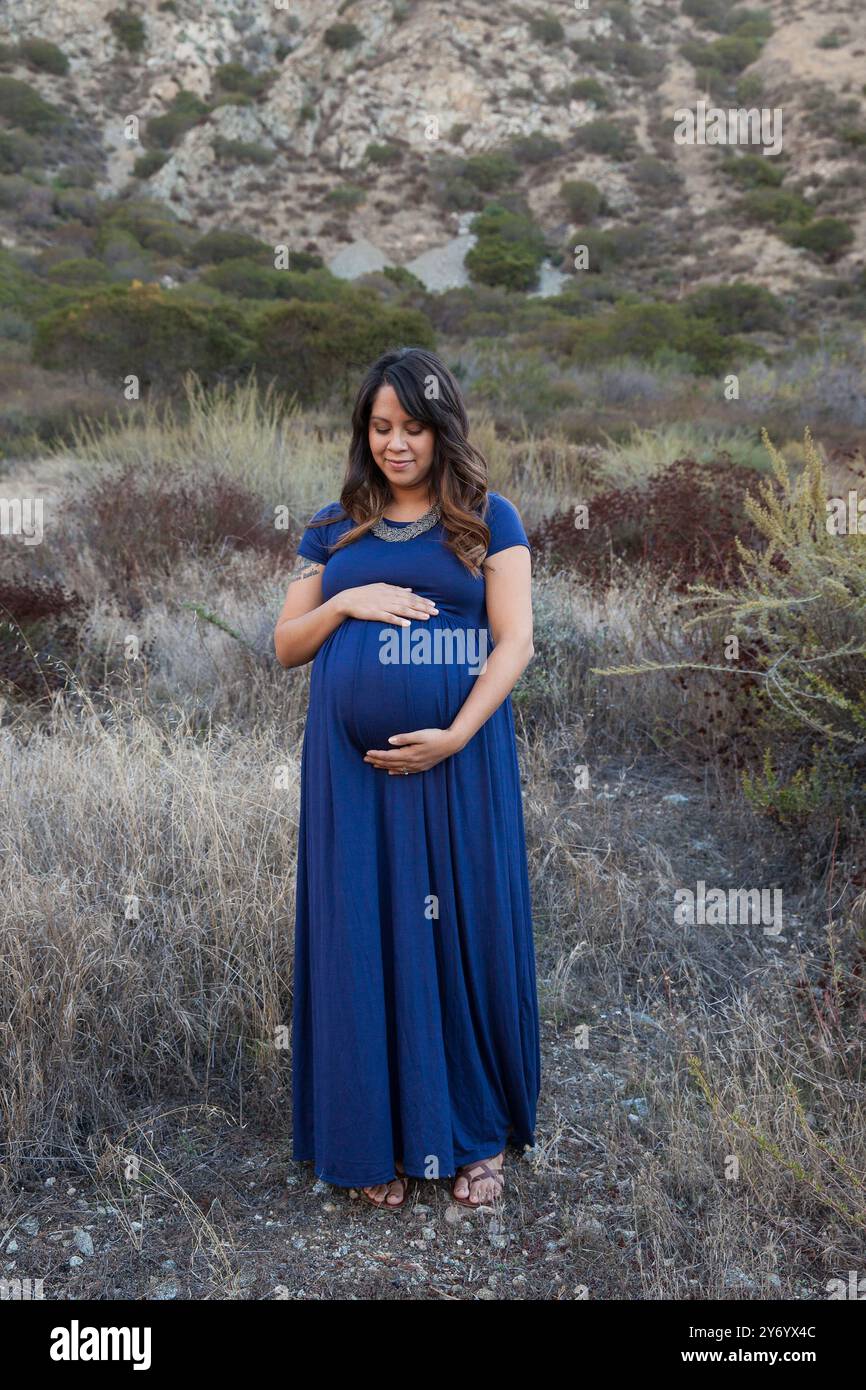 Femme enceinte dans une robe bleue berçant son ventre dans la nature Banque D'Images