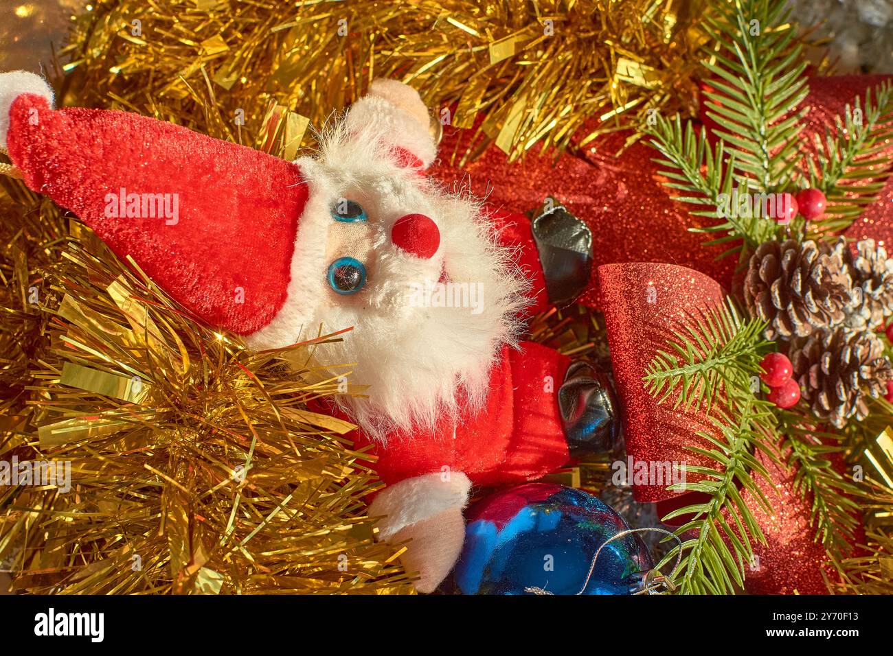 Jouet en peluche du Père Noël assis au milieu d'une scène de Noël festive. La figure du Père Noël, avec sa barbe blanche moelleuse, son costume rouge vif et ses yeux bleus, est surr Banque D'Images