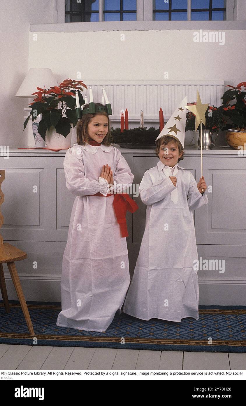 Princesse héritière Victoria et son frère le prince Carl Philippe de Suède 1984. Vêtu d'une tenue traditionnelle lors de la célébration de la Saint Lucy le 13 décembre. On voit la reine Silvia aider sa fille à s'habiller. Banque D'Images