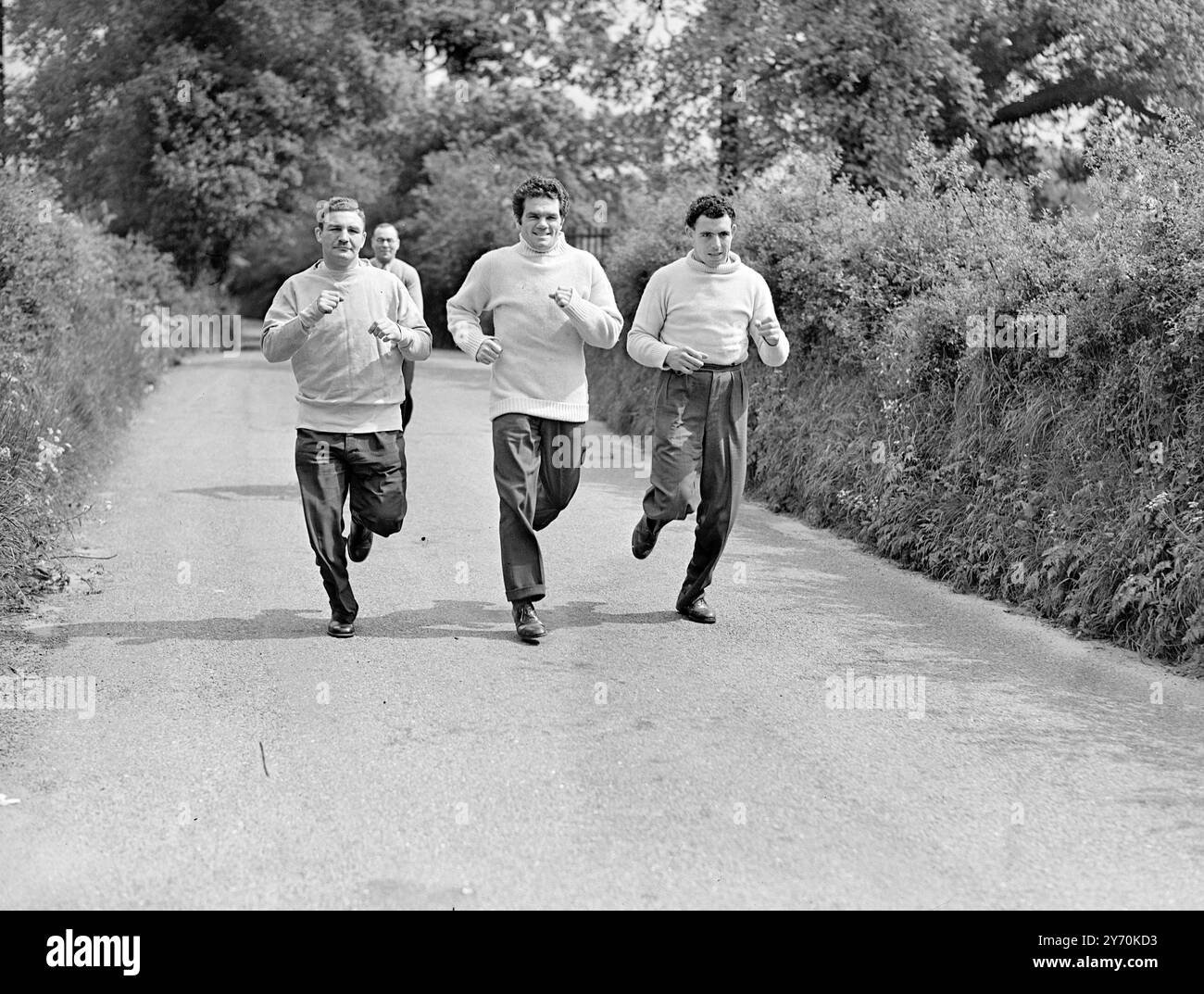 MILLS COMMENCE LA FORMATION FINALE Freddie Mills , champion du monde léger - poids lourds , est entré dans les dernières étapes de la formation pour son combat avec Bruce Woodcock quand il a déménagé de sa maison Brixton ( Londres ) aux quartiers d'entraînement de pays à la Mow d'orge , Betchworth , Surrey . Mills tentera de priver Woodcock de ses titres de poids lourds britanniques , européens et impériaux à la White City , Londres , le 2 juin . L'IMAGE MONTRE :- FREDDIE MILLS ( au centre) sur une course d'entraînement à Betchworth avec les partenaires de sparring KEN SHAW ( à gauche ) , champion poids lourds d'Écosse , et JOHNNY WILLIAMS de Barmou Banque D'Images