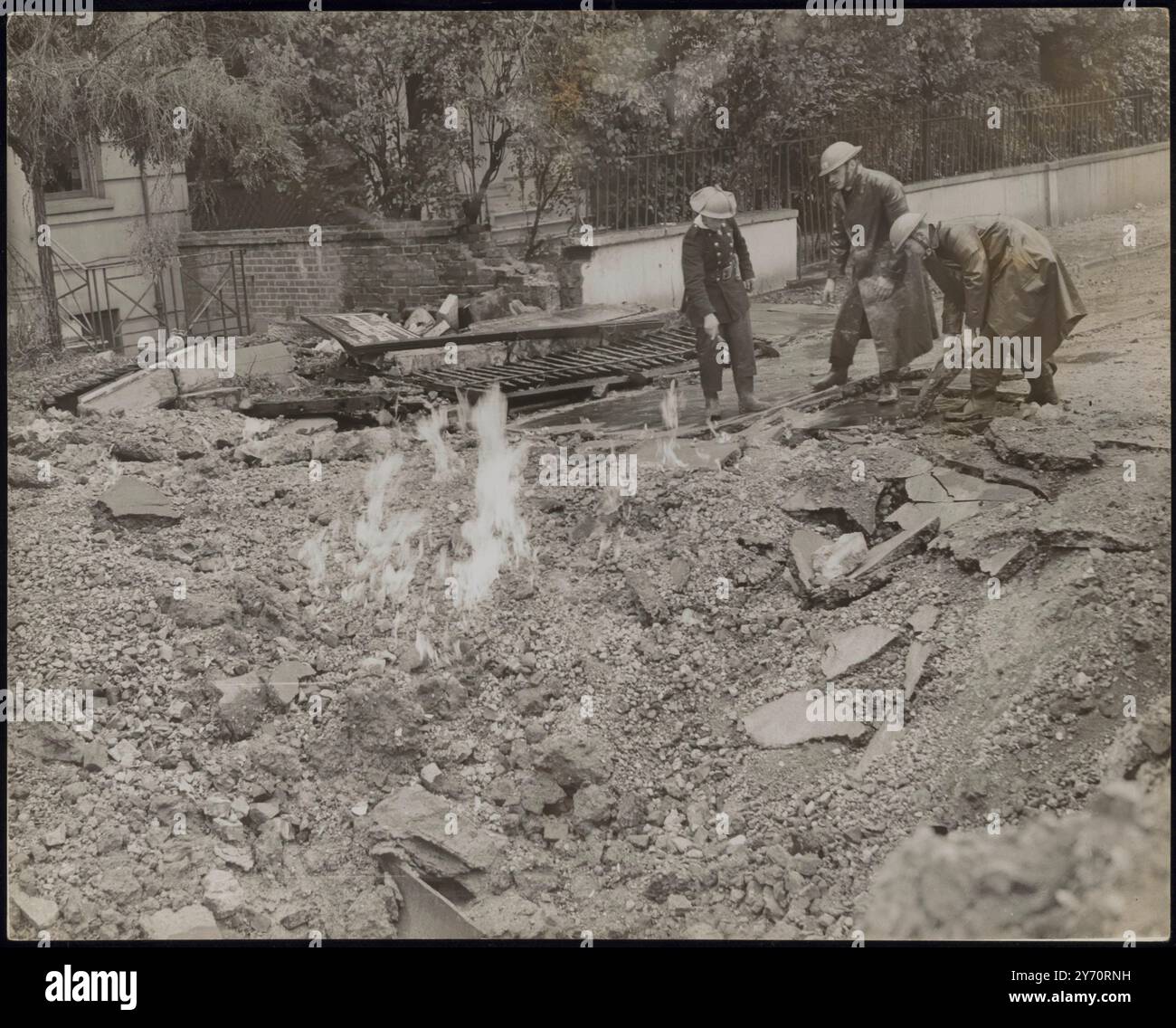 CINQ CENTS PERSONNES S'ÉCHAPPENT QUAND UNE BOMBE EXPLOSE PRÈS D'UN ABRI. 500 personnes dans un abri anti-aérien n'ont pas été blessées lorsqu'une bombe explosive élevée larguée par des raids nazis dans la région de Londres a explosé à un endroit entre l'abri, un garage et une église. Une voiture a été soufflée à travers le toit du garage et dans la rue. LA PHOTO MONTRE:- le cratère fait par la bombe. Les flammes sont causées par une conduite de gaz cassée. 10 septembre 1940 CENSEUR N° 67917 Banque D'Images