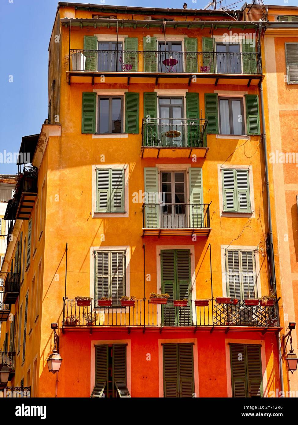 Immeuble méditerranéen coloré avec volets et balcons traditionnels, baigné de lumière chaude du soleil. Scène de rue dynamique dans le sud de l'Europe - Image de stock capturée avec un smartphone