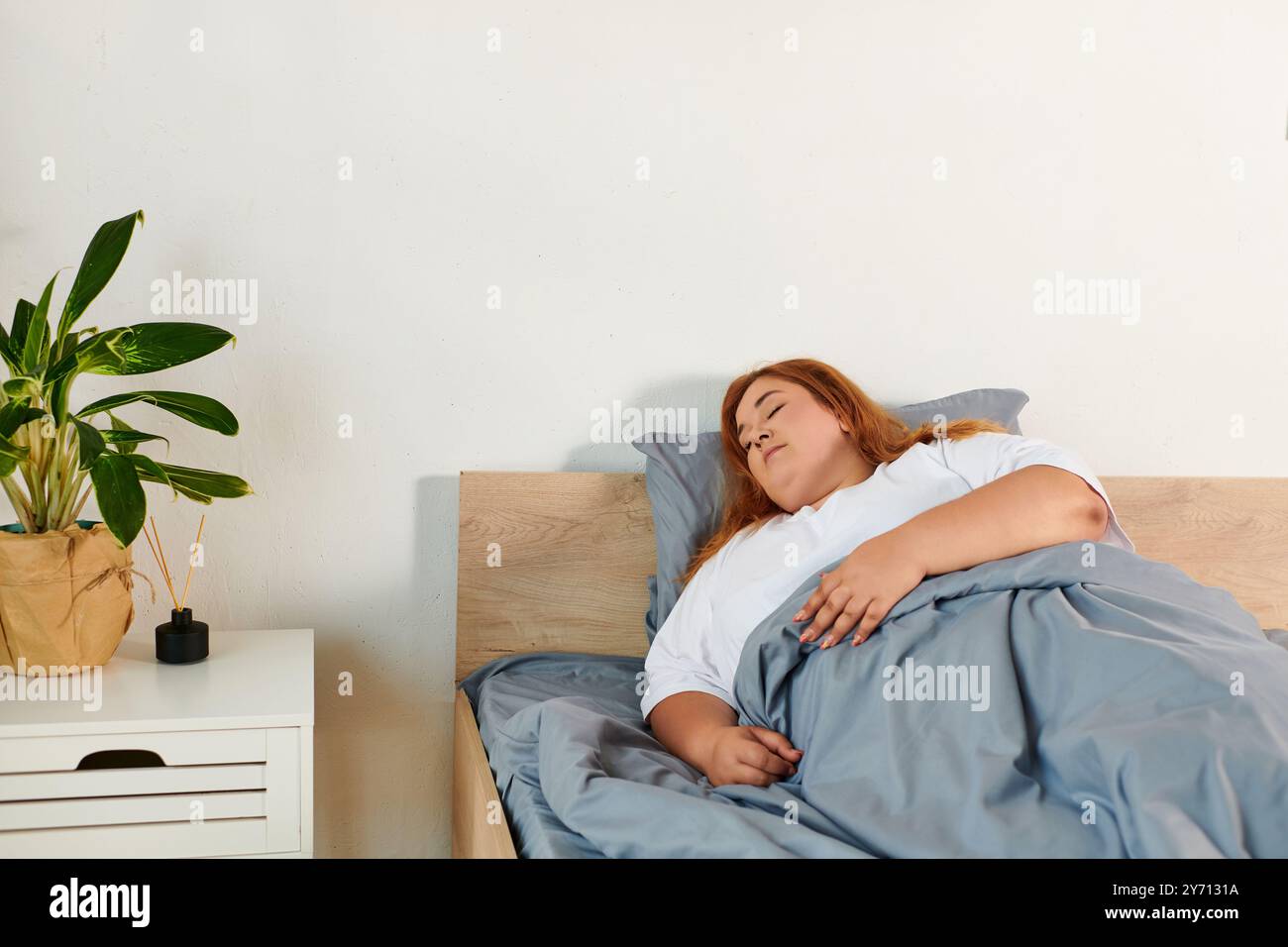 Une belle femme de grande taille se repose calmement dans son lit, enveloppée dans des couvertures douces, exsudant la tranquillité. Banque D'Images