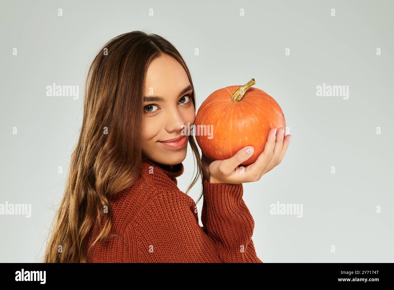 Une belle femme aux cheveux longs pose joyeusement, berçant une citrouille vibrante dans ses mains. Banque D'Images