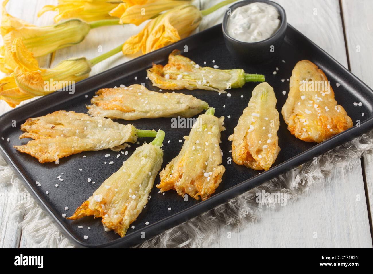 Fleurs de courgettes panées frites maison saupoudrées de gros sel gros plan dans une assiette sur une table. Horizontal Banque D'Images