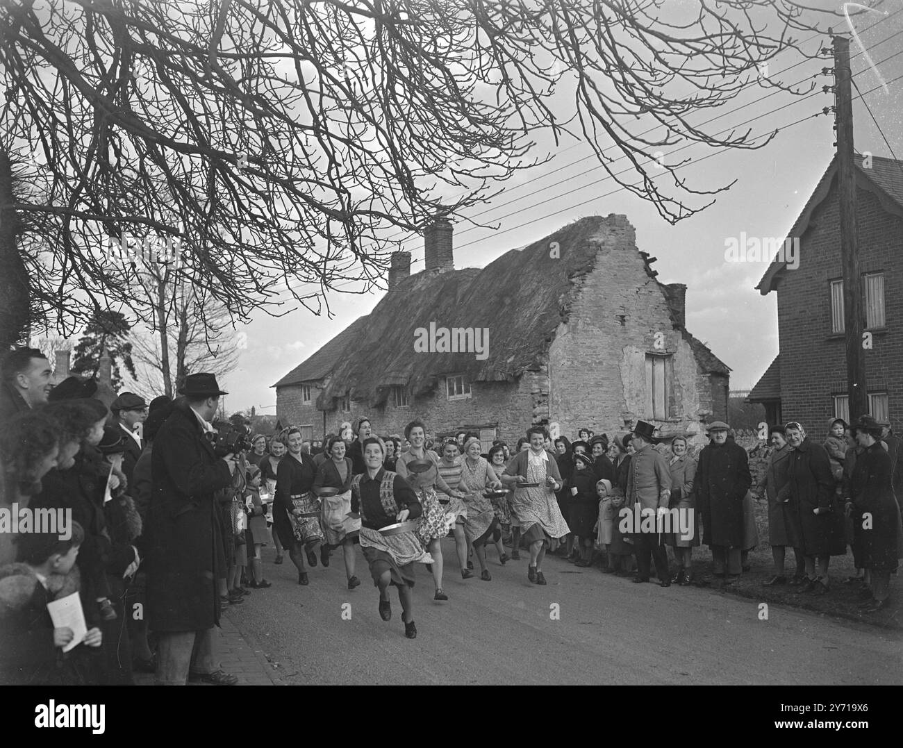 CASSEROLES AU PREMIER PLAN avec des poêles à frire à la ''alerte'' les ménagères d'Olney , Bucks , courent à travers le village en passant un vieux chaume cottage sur leur route . Il y a 500 ans, les ménagères de ce village ont d'abord couru de leurs maisons avec des crêpes à l'église du village pour recevoir le ''baiser de Pace'' et la bénédiction des victoires. aujourd'hui, c'était la 2ème fois que la cérémonie était - re - promulguée . 1er mars 1949 Banque D'Images