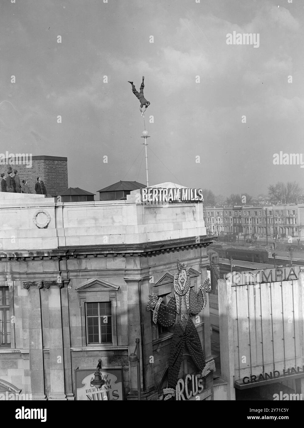 JOLLY HIGH ! '' JOLLY '' , ou pour lui donner son nom propre JOHAN PICHLER , un australien se produisant au Bertram Mills Circus , a décidé qu'il ne serait pas dépassé par les récents exploits d'escalade Eres alors il est allé '' droit au poteau '', non seulement au-dessus du cirque mais au-dessus du bâtiment lui-même ., à Olympia , Londres , en s'équilibrant à 60 pieds au-dessus de la circulation sur un poteau de 15 pieds érigé sur le coin supérieur du bâtiment . Même alors, ses ambitions les plus élevées n'ont pas été réalisées , pour avoir placé son bâton de marche de cirque au sommet de la balle qui surmonte le poteau , il a procédé à l'équilibre Upside dow Banque D'Images