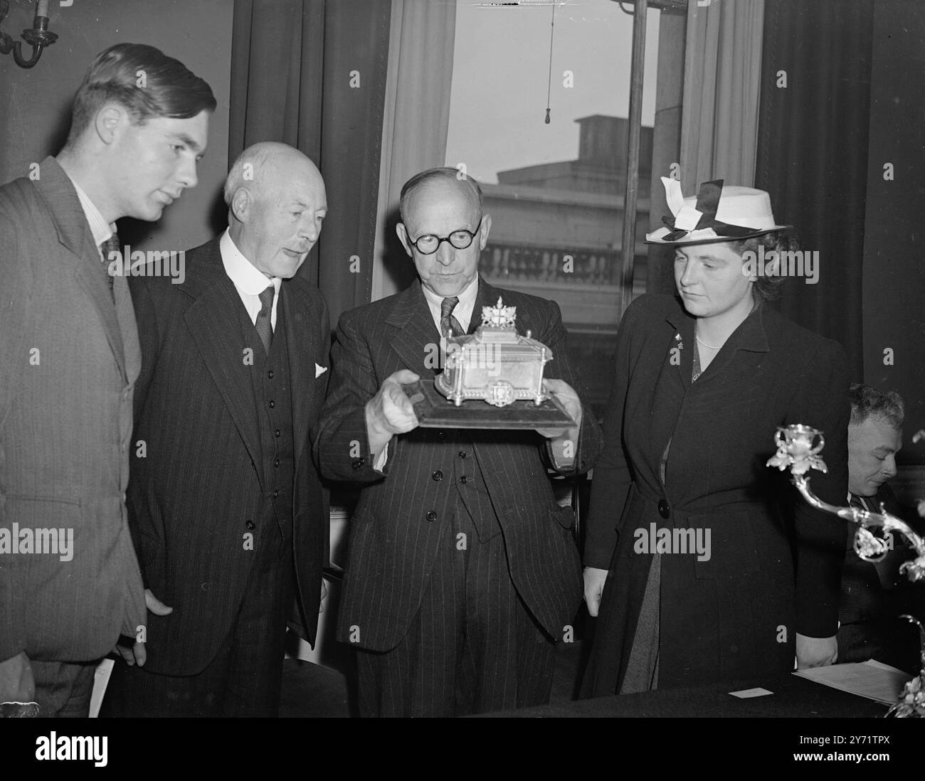 Cadeau plaque d'argent pour le bureau de poste. Une cérémonie informelle a eu lieu dans la salle à manger du maître des postes, dans le bâtiment du Siège, à Londres, lorsqu'une collection de plaques d'argent d'une valeur considérable et d'un intérêt historique a été présentée à la poste. La collection qui a été présentée à Sir Rowland Hill au cours de sa vie pour son travail sur la réforme postale, a été offerte à la poste par ses petits-fils, le colonel W Hill et le major d'Estree. Images : le RT Hon Wilfred Paling, député, (deuxième à partir de la gauche) le ministre des postes, inspectant un cercueil argenté doré contenant le Free Banque D'Images