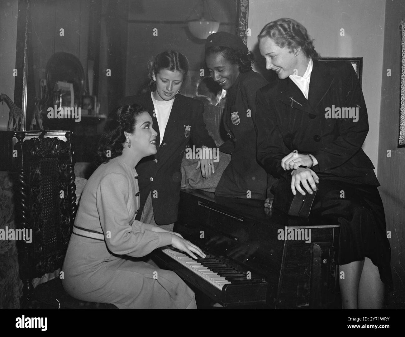 Athlète AMÉRICAINE rencontrez Anna les athlètes olympiques américaines forment un public admiratif tandis que Hilda Simms, star de la pièce « Anna Lucasta » leur donne un air sur son piano dans son vestiaire pendant l'intervalle de matinée d'aujourd'hui. De gauche à droite, Jackie la Vine (équipe olympique américaine de natation) Alice Coachman (saut en hauteur olympique), Janice Lee de York, (équipe olympique américaine d'escrime) photographiée au His Majesty's Theatre, Londres. 11 août 1948 Banque D'Images