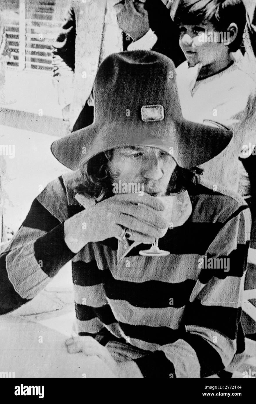 Rolling Stone Mick Jagger , vêtu d'un chapeau souple et large, d'une broche dorée et d'une chemise rayée orange et noire , avec un pantalon rose , prend un verre au salon de la piscine de l'hôtel Copacabana de Rio le 11 janvier 1968 Banque D'Images