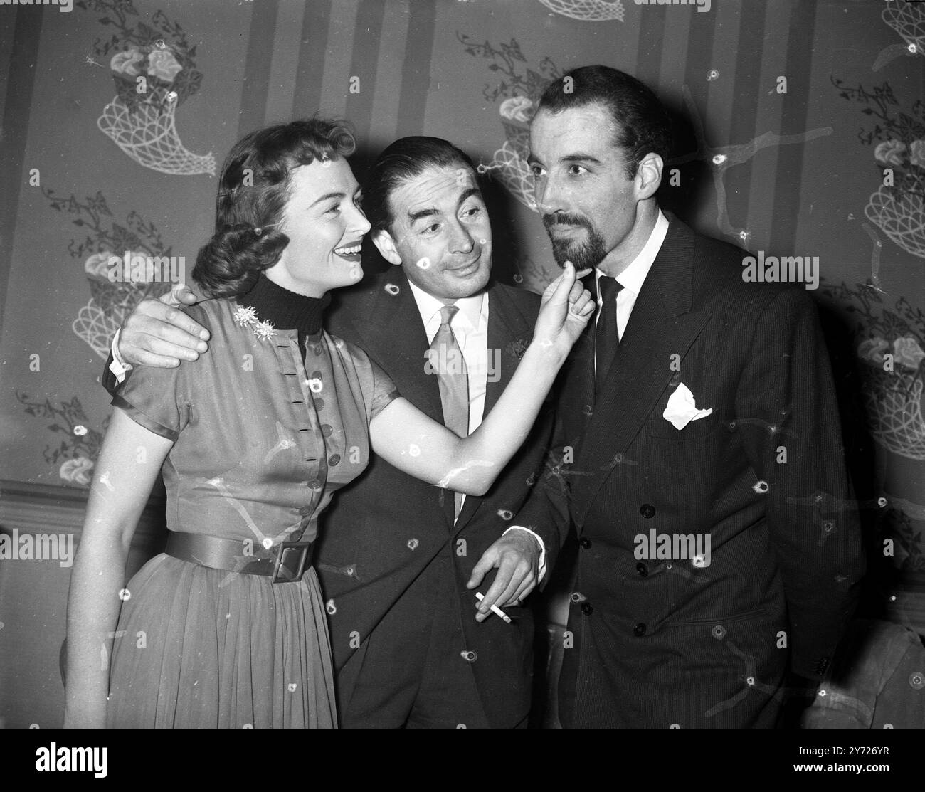 'Beyond Mombasa' stars ont Londres se réunir. L'acteur Christopher Lee (à droite) se fait tweeter la barbe par la glamour Donna Reed tandis que Leo Genin regarde la réception de presse au Savoy Hotel de Londres pour lancer le nouveau film 'Beyond Mombasa' dans lequel ils jouent avec Cornel Wilde . Le film sera tourné au Kenya sous la direction de George Marshall . 5 janvier 1956 Banque D'Images