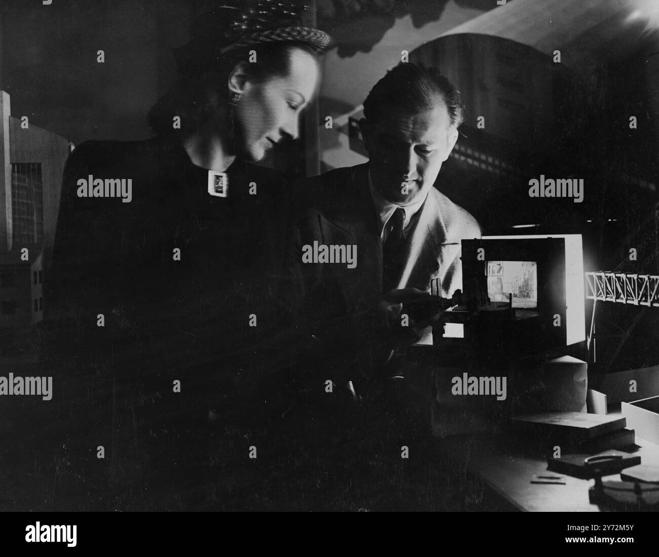 Parfois, le personnel de studio est expert en effets illusoires. Ici, David Rawnsley démontre un ensemble d'interverrouillage ; finalement, le principe, déjà utilisé, sera largement appliqué. La scène latérale éliminée patrouillant dans les rues représente un film pré-capturé ; le petit ensemble supplémentaire correspond au premier plan en direct. Les deux, en tricotant ensemble, complètent le réglage. Actuellement, il est filmé ; finalement, il sera télévisé. 2 avril 1947 Banque D'Images Parfois, le personnel de studio est expert en effets illusoires. Ici, David Rawnsley démontre un ensemble d'interverrouillage ; finalement, le principe, déjà utilisé, sera largement appliqué. La scène latérale éliminée patrouillant dans les rues représente un film pré-capturé ; le petit ensemble supplémentaire correspond au premier plan en direct. Les deux, en tricotant ensemble, complètent le réglage. Actuellement, il est filmé ; finalement, il sera télévisé. 2 avril 1947 Banque D'Images