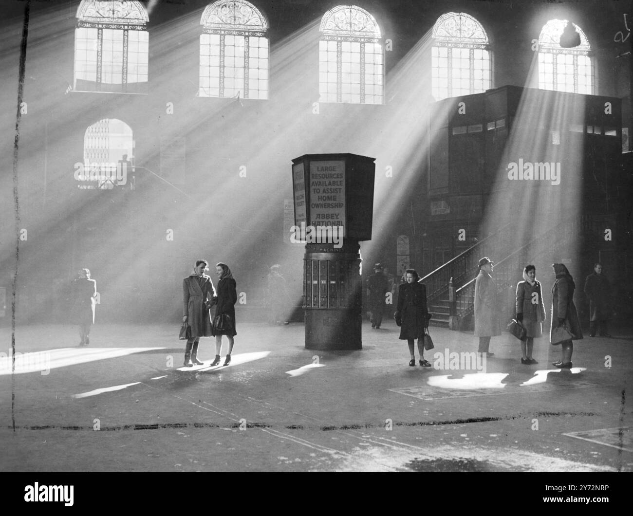 Une place au soleil. Le soleil éclatant traverse le toit vitré pour percer la morosité à Liverpool Street Station ce matin alors que le temps printanier a déplacé les conditions hivernales récentes. Les passagers qui attendent le train ont mis le terminus ce matin (mercredi). 26 février 1947 Banque D'Images