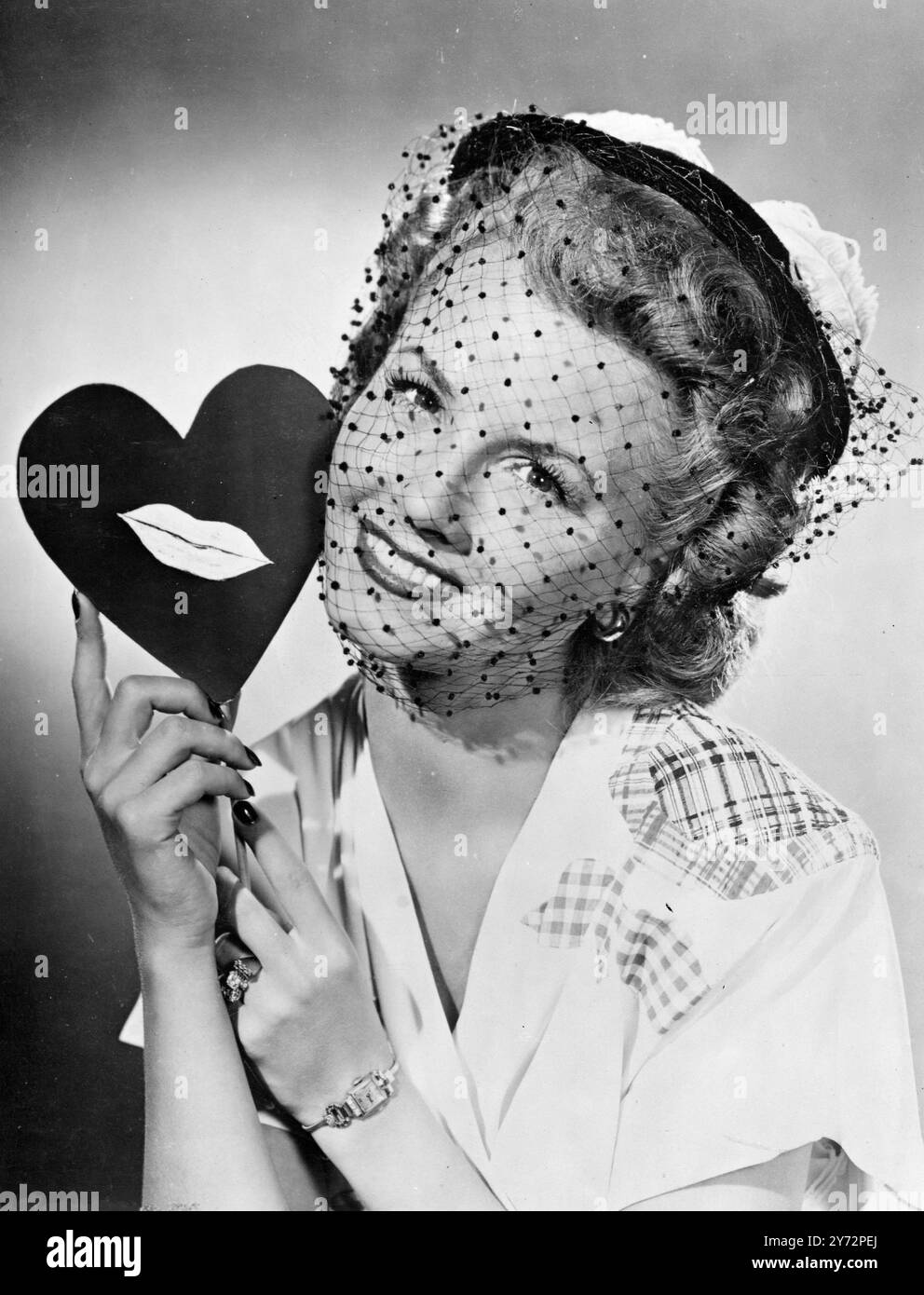 Valentine moderne. Séduisante Janet Blair, star de Columbia, envoie cette charmante Saint-Valentin d'Hollywood pour la Saint-Valentin du 14 février, un cœur symbolique barbant ses empreintes de lèvres ! Note de mode, Janet hors du visage chapeau de marin de paille noir, a une plume bleu pâle sur la couronne, bord retourné avec voile large de tache de maille. Sa robe en crêpe bleue comme motifs de fleurs sur le devant multicolore. 12 février 1947 Banque D'Images
