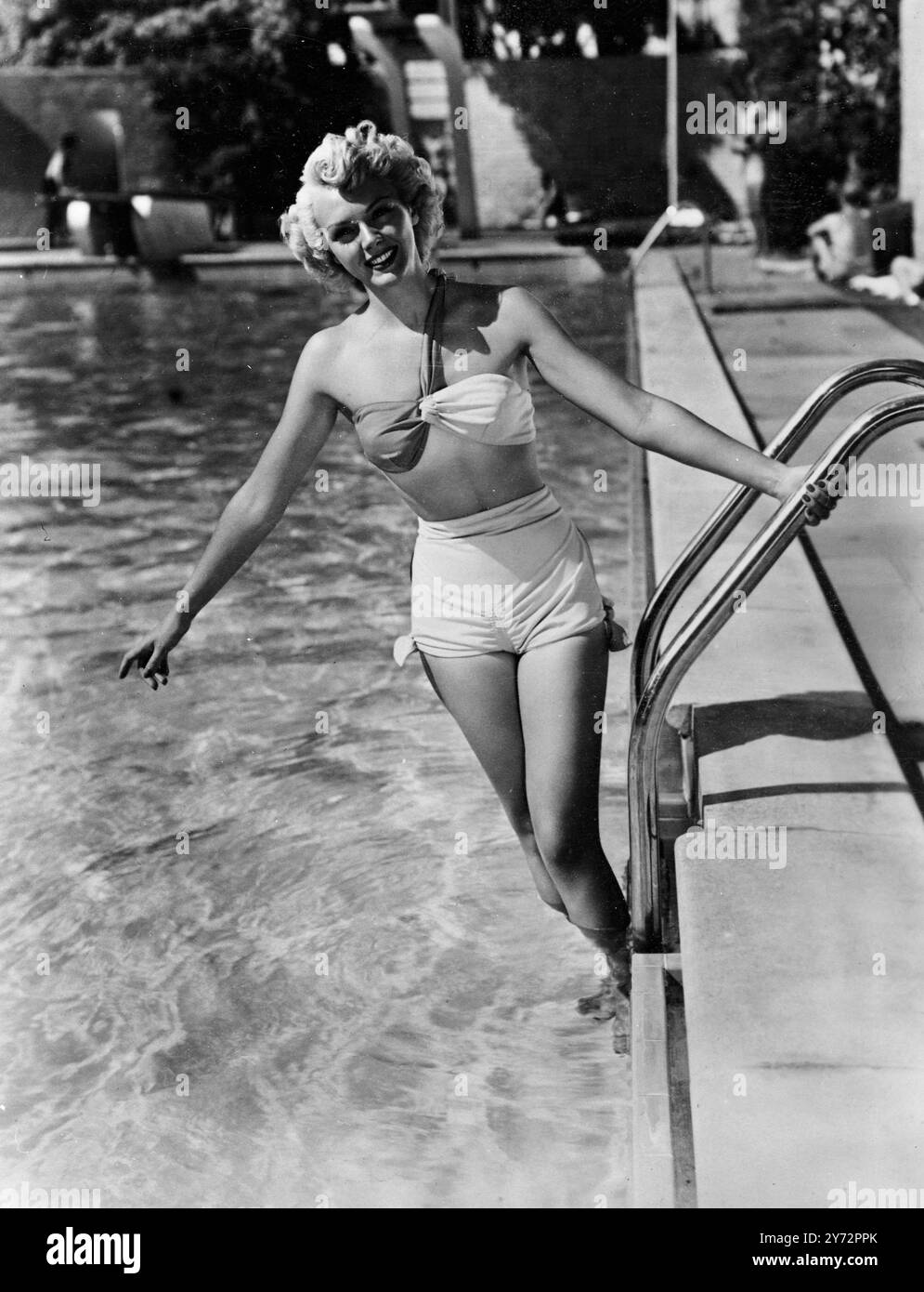 Confort par temps froid. Tandis que la Grande-Bretagne fait le tour avec son col vers le haut, Leslie Brooks, star de Columbia Pictures, pour apporter une lueur de chaleur bienvenue à la perspective enneigée. Sur cette photo, prise sous le soleil californien, Leslie, porte un maillot de bain en plastique nouveau style de teinte vert et jaune pastel. Le haut de soutien-gorge à une sangle , et les noeuds soignés sur les troncs sont des caractéristiques remarquables. 27 janvier 1947 Banque D'Images