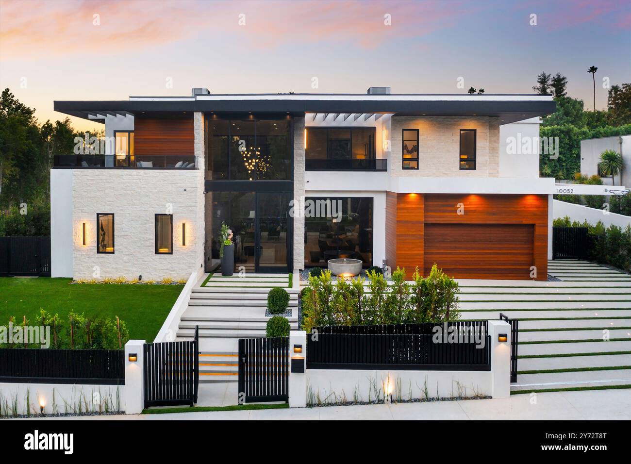 Une maison de luxe moderne avec de grandes fenêtres, une pelouse bien entretenue et un ciel de coucher de soleil en arrière-plan. Banque D'Images