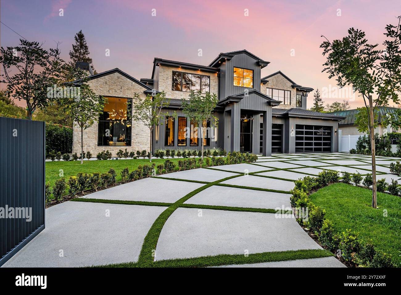 Extérieur de maison de luxe moderne avec une pelouse bien entretenue, allée géométrique et ciel de coucher de soleil en arrière-plan. Banque D'Images