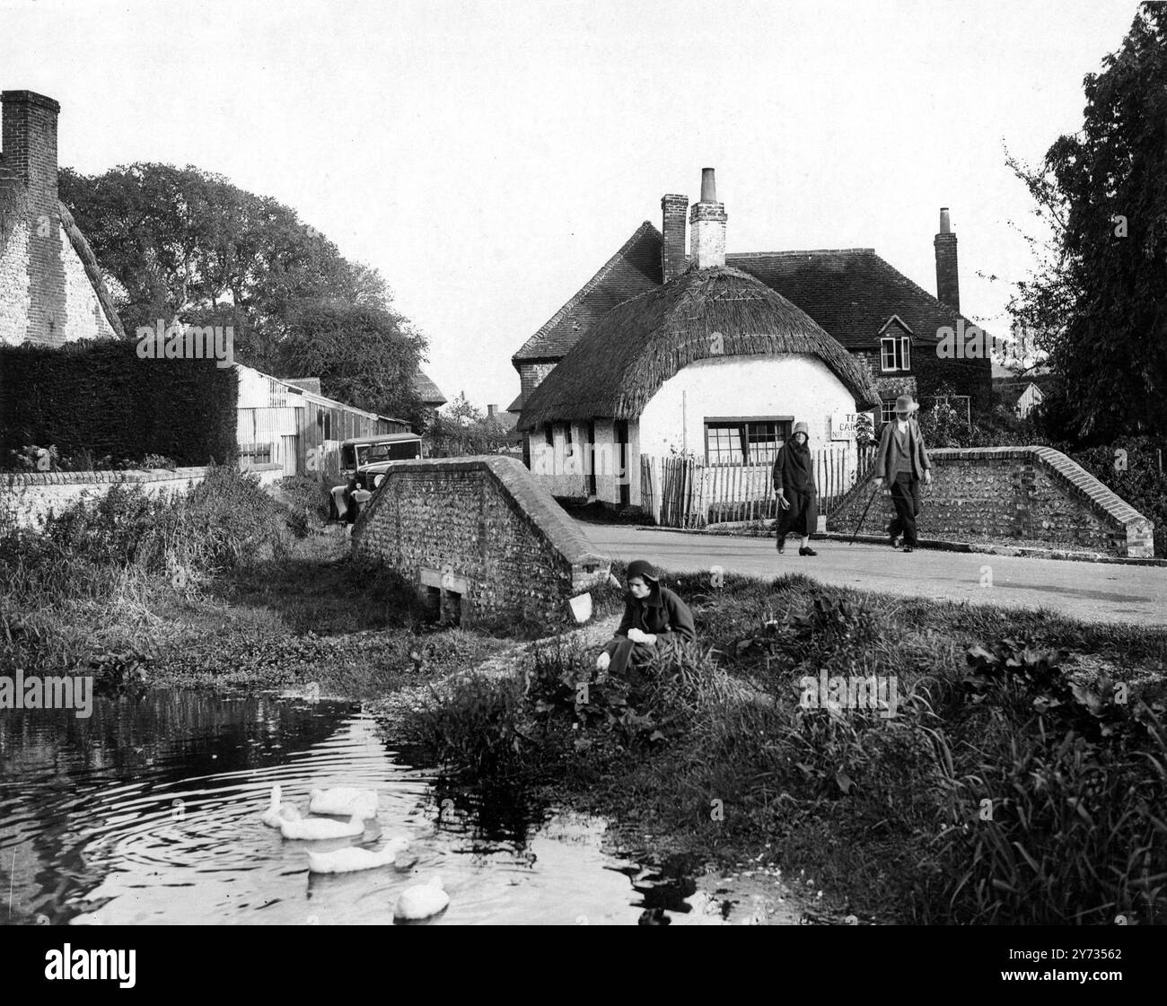 Le vieux cottage au toit de chaume , le ruisseau ondulant , et une jolie fille nourrissant les canards se combinent pour faire une image charmante de la campagne anglaise au début de l'automne . Cette photo est de Singleton , près de Goodwood , West Sussex , Angleterre . 14 octobre 1931 Banque D'Images