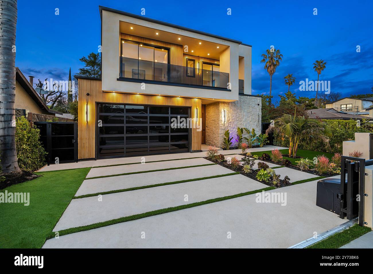 Maison moderne de deux étages avec de grandes fenêtres, une cour avant bien entretenue et des palmiers au crépuscule. Banque D'Images