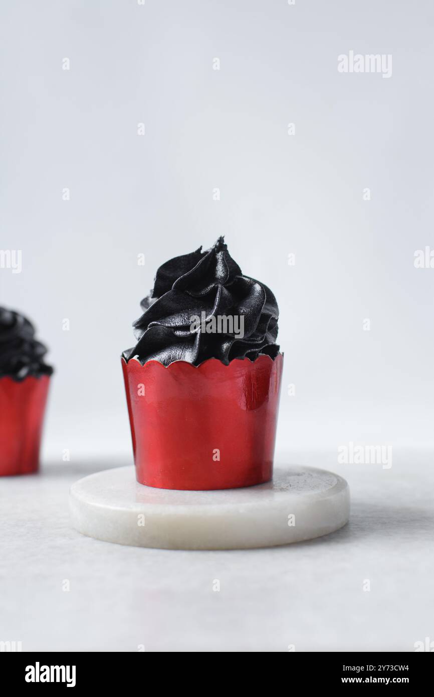 Cupcakes rouges avec tourbillon noir de crème au beurre, cupcakes dans des doublures rouges de feuille avec crème au beurre noir, cupcakes de valentines glacés d'Halloween sur un dos blanc Banque D'Images