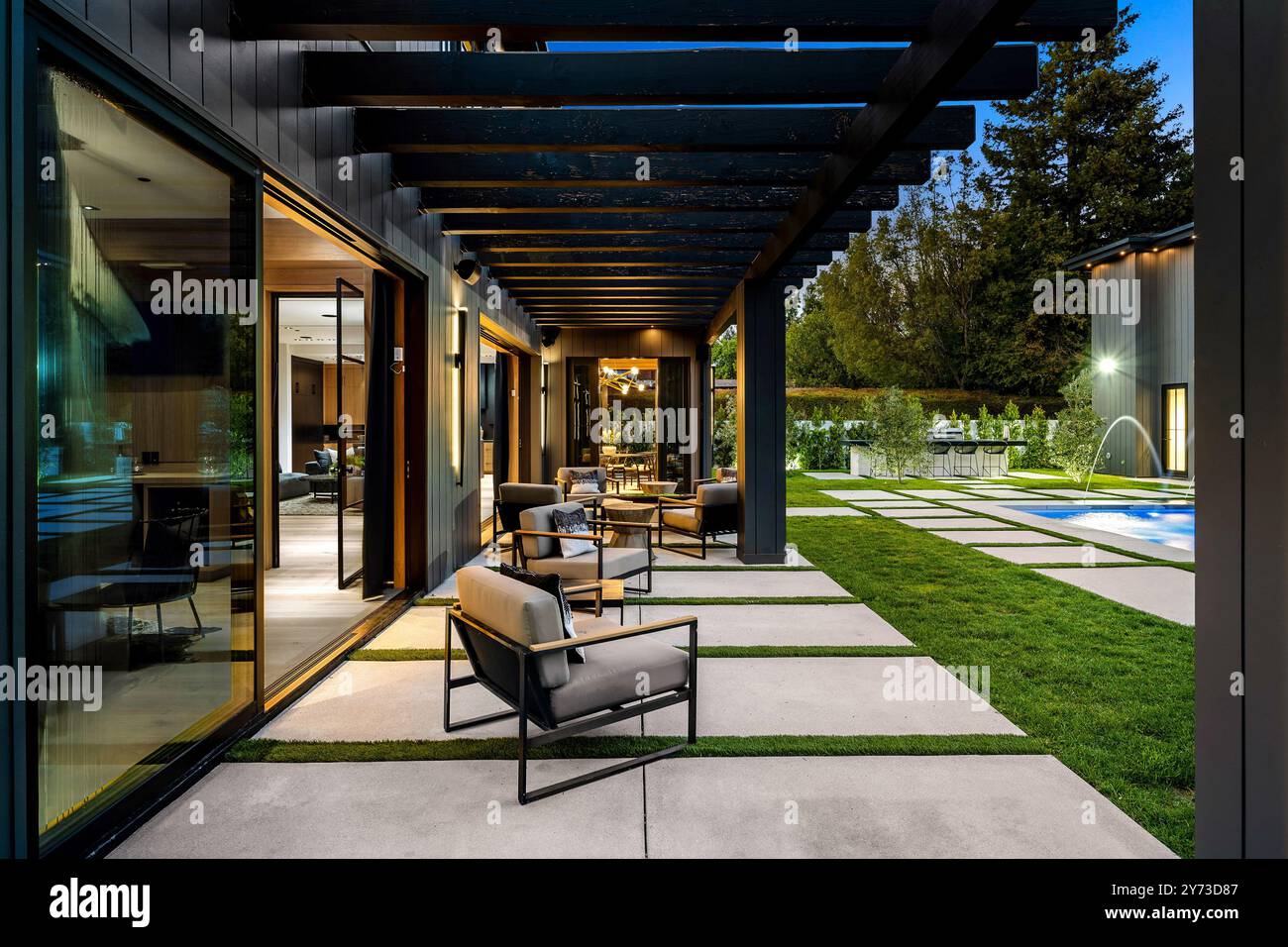 Patio extérieur moderne avec sièges confortables, pergola et pelouse bien entretenue à la lumière du soir. Banque D'Images