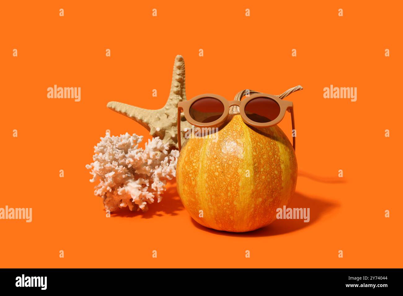 Citrouille avec corail, étoile de mer et lunettes de soleil sur fond orange Banque D'Images