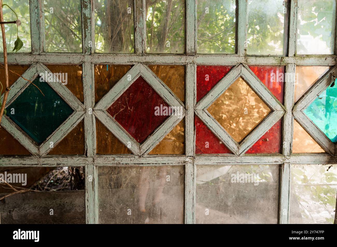 Fenêtre en verre magnifiquement vieilli avec des motifs colorés Diamond encadrés par la nature. Banque D'Images