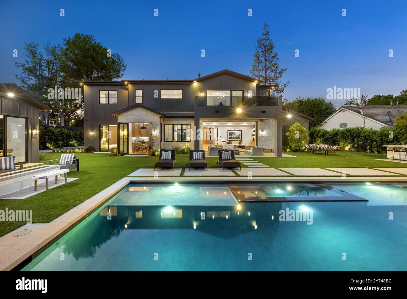 Luxueuse maison moderne avec piscine et pelouse bien entretenue, capturée au crépuscule. Banque D'Images