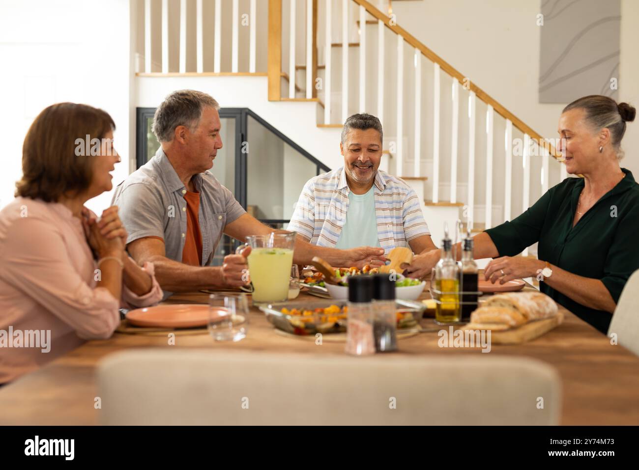 Profiter du repas, amis seniors divers assis autour de la table à manger, partager de la nourriture et des boissons, à la maison Banque D'Images