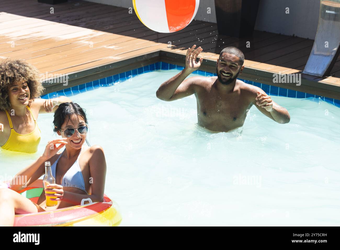 Jouer avec le ballon de plage dans la piscine, divers amis appréciant le repaire d'été ensemble, à la maison Banque D'Images